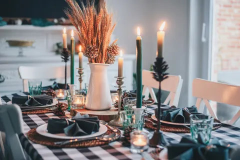 Cozy autumn dining table with black and white checkered cloth, candles, wheat centerpiece, and rustic tableware.