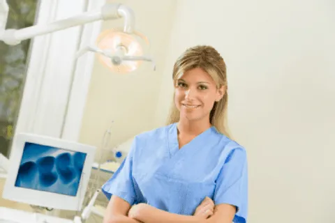 Smiling female dental assistant in blue scrubs in a dental office setting.