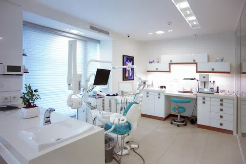 Bright modern dental clinic with dental chair, monitor, sink, and white cabinetry under natural light.