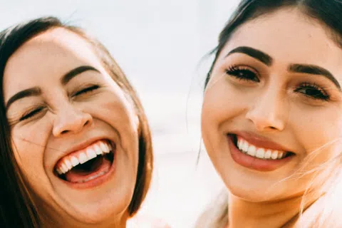 Two young women smiling and laughing outdoors, close-up portrait capturing joy and friendship.