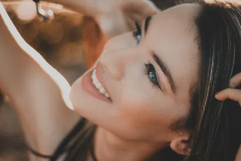 Close-up of a smiling young woman with smooth skin and dark hair in warm natural light.