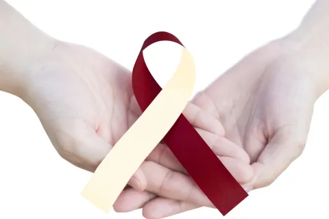Two hands holding a maroon and cream awareness ribbon, symbolizing support and advocacy.
