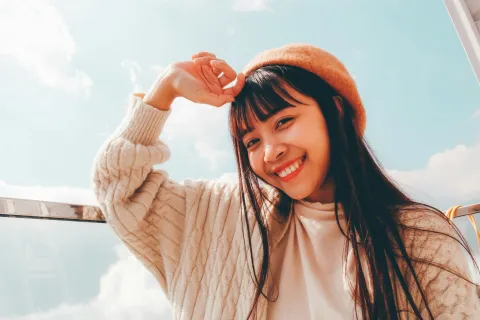 Smiling woman wearing a beret and cozy sweater against a bright sky backdrop.