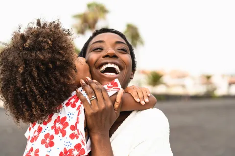 Joyful mother and child sharing a loving moment on a sunny beach, captured in a warm and playful embrace.