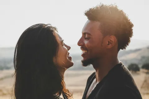 Smiling couple looking at each other outdoors in a sunlit natural setting with hills in the background