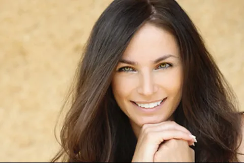 Smiling woman with long dark hair, showcasing a warm and inviting expression against a neutral background.