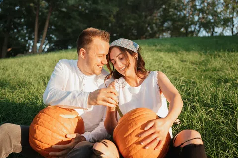 Couple carving pumpkins together outdoors on a sunny day in a grassy field during autumn season.