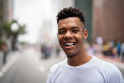 Smiling young man with braces, wearing a white shirt in an urban setting with blurred background.