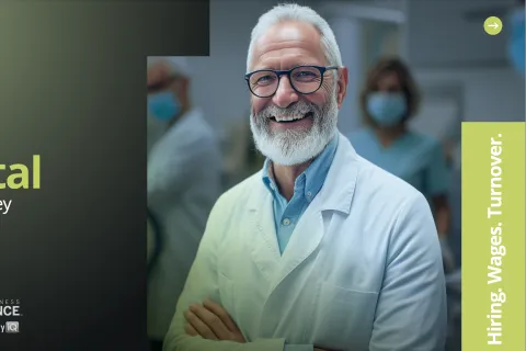 Smiling senior male dentist in white coat with team in background for 2026 dental salary survey report.