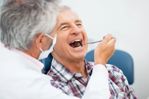 Dentist performing an oral check-up on a smiling senior man in a dental clinic.
