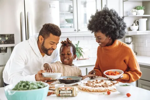 Family of three enjoying cooking together in a bright modern kitchen preparing a pizza meal.