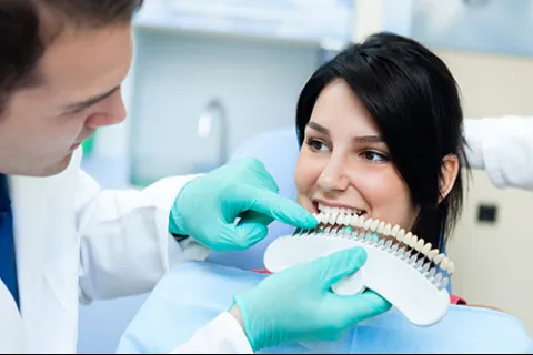 Dentist showing woman a tooth shade guide to match her teeth color during dental appointment