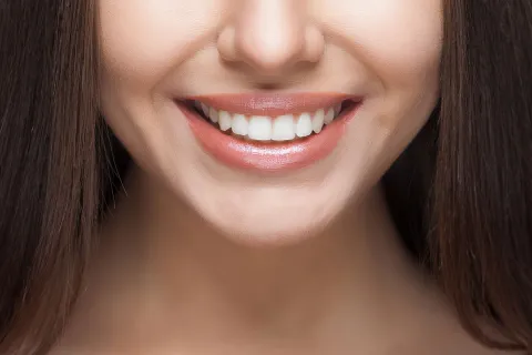 Close-up of a woman's smiling face highlighting bright, healthy teeth and glowing skin.
