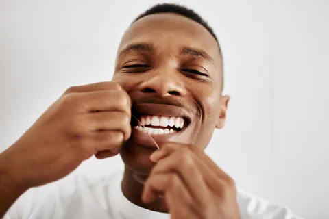 Smiling man using dental floss to maintain oral hygiene and healthy teeth.
