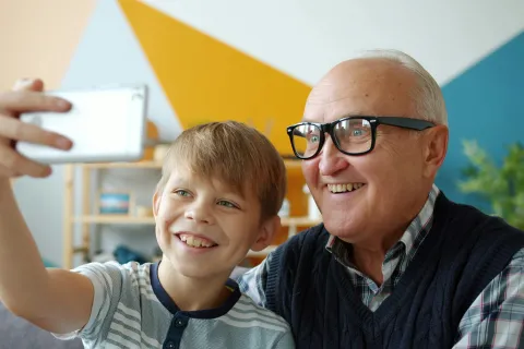 Young boy and elderly man smiling as they take a selfie together indoors with colorful geometric wall background.