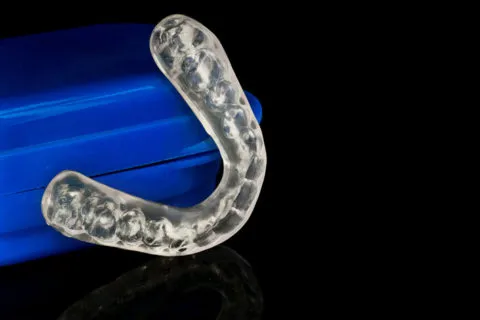 Clear mouthguard beside a blue protective case on a black reflective surface.
