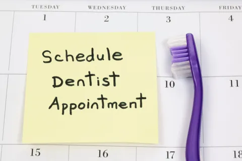 Sticky note reminder for scheduling a dentist appointment next to a toothbrush.
