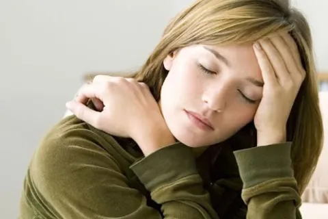 Young woman with eyes closed, resting her head on hand, appearing tired or stressed indoors.