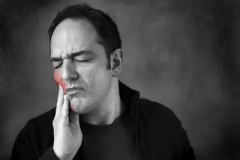Man grimacing in pain, touching his jaw to indicate toothache or dental discomfort.