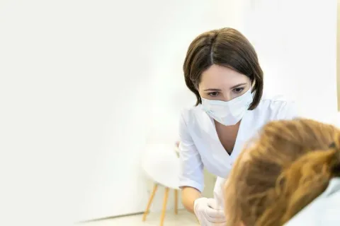 A healthcare professional in a mask attentively examines a patient in a clinical setting.
