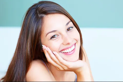 Smiling young woman with long brown hair resting her chin on her hand, showcasing a joyful expression.
