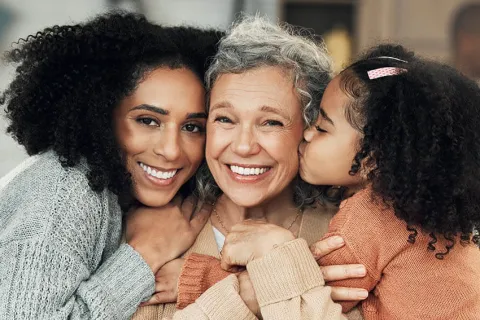 Three generations of women smiling together, showcasing love and family bonds in a cozy indoor setting.