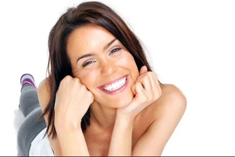 Smiling woman with bright white teeth lying down with hands under chin on white background
