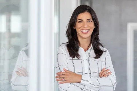 Confident businesswoman smiling with arms crossed in a modern office setting.