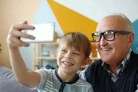 Smiling grandfather and grandson taking a selfie together in a colorful living room with geometric wall art.