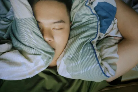 Person sleeping peacefully under green and white striped blanket with arm resting beside head