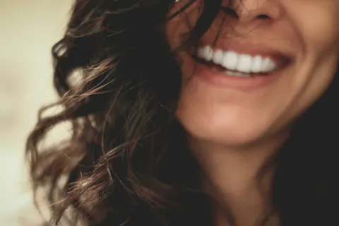 Close-up of a smiling woman with curly dark hair showing white teeth and joyful expression.