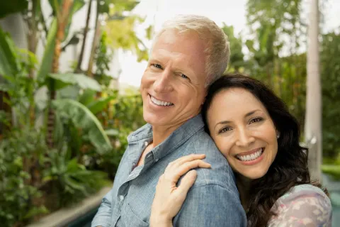 Happy mature couple embracing outdoors in a lush green garden with smiles, showing affection and warmth.