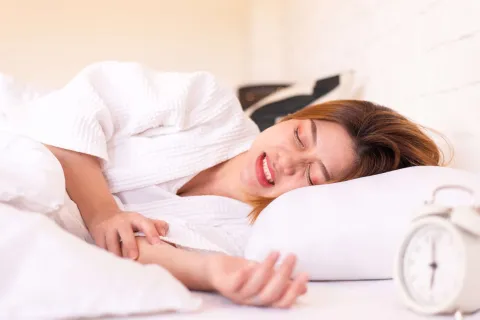 A woman in a bathrobe experiencing discomfort while lying in bed.
