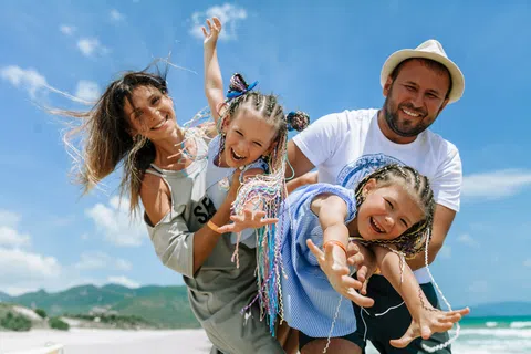 Happy family of four playing on the beach with blue sky and ocean in the background