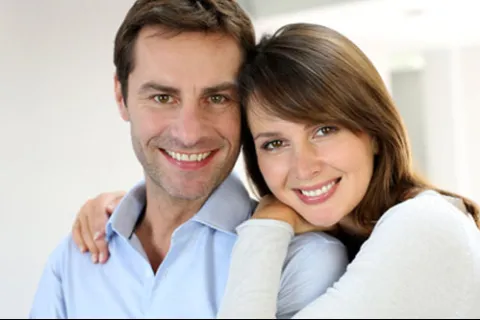 Smiling couple embracing indoors with casual clothing and warm expressions.
