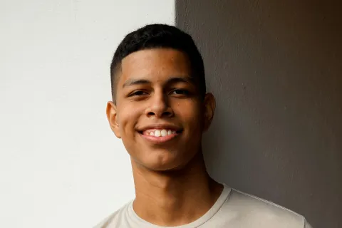 Smiling young man in a light beige t-shirt standing against a wall with white and dark brown sections.