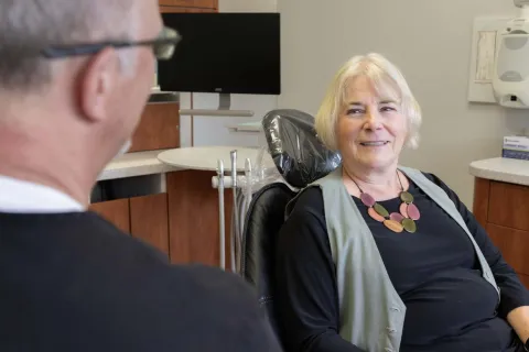 Senior woman smiling while sitting in dental chair talking to dentist in modern clinic.