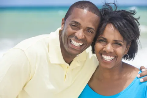 Happy smiling African American couple posing together at the beach with ocean in the background.