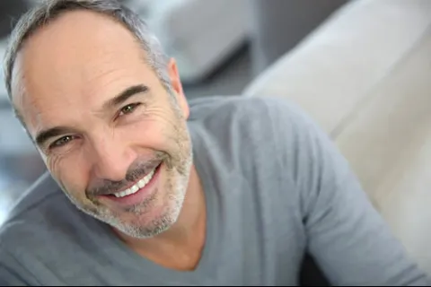 Smiling middle-aged man with a gray sweater, relaxed in a modern living room.