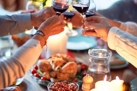 Friends clinking wine glasses over a festive dinner table with roasted chicken and lit candles.