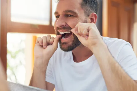 Man flossing his teeth at home in a well-lit bathroom, focusing on dental hygiene.