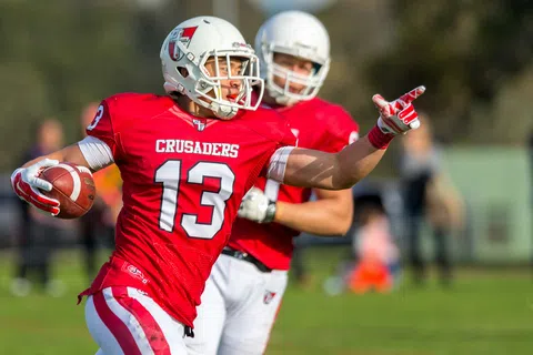 Football player in red Crusaders uniform with number 13 running with ball and pointing during game