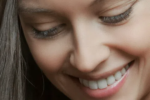 Close-up of a smiling woman with long dark hair and clear skin looking down.