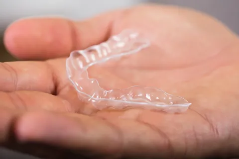 A person holding a clear dental retainer in their hand, showcasing its transparent design.