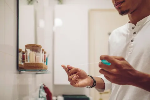 A man using dental floss in a bathroom setting, promoting oral hygiene and wellness.