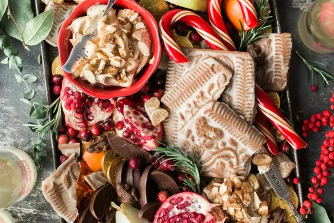 Festive tray with assorted holiday treats including gingerbread, candy canes, pomegranate, chocolate, and fresh fruit.