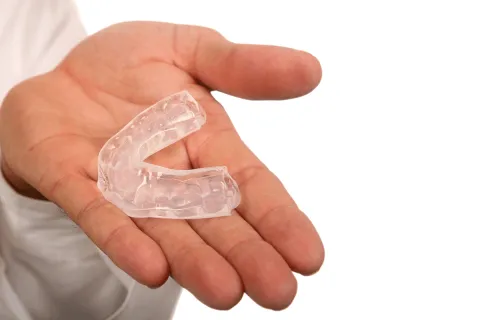 A person holding a clear dental mouthguard in an open hand against a white background.