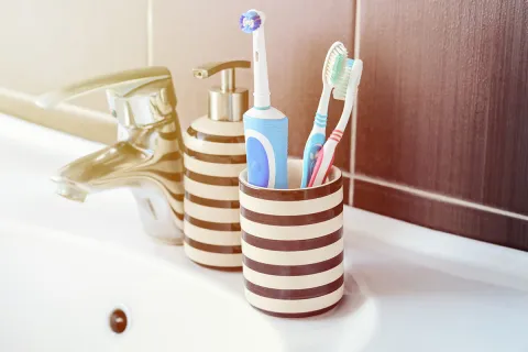 Stylish bathroom accessories with striped holder, toothbrushes, and electric toothbrush near faucet.