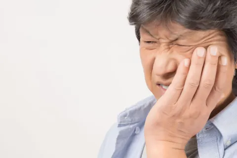 A person grimacing in pain, holding their jaw, indicating a toothache or dental discomfort.