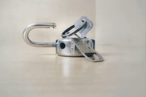 Close-up of an open silver padlock with a key inserted on a neutral background.